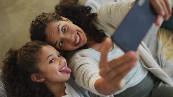 Happy mixed race mother and daughter laying on the floor,having fun and taking selfie