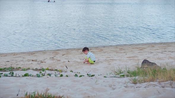 Happy and Carefree Child Plays By the Sea, Picks Up Sand with a Spatula, Pours Sea Water Into a