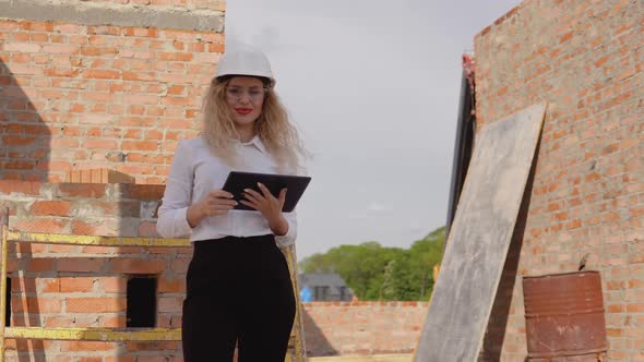 Female Architect in Business Attire Stands in a Newly Built House with Untreated Walls and Works on