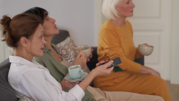Laughing mature women switching channels and drinking tea