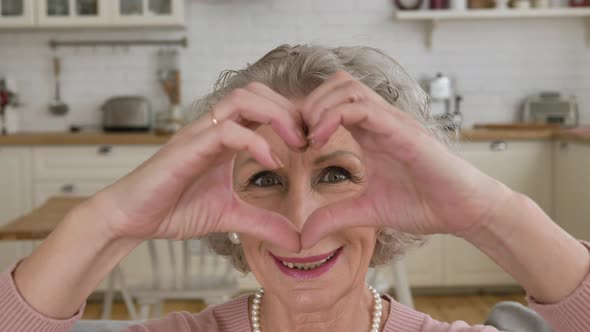 Pensioner with Short Grey Haircut Holds Hands in Heart Shape