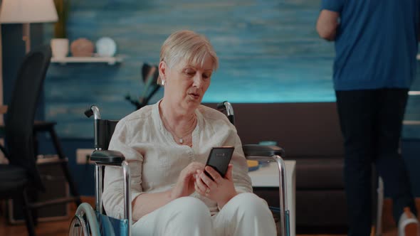 Senior Person Sitting in Wheelchair and Using Smartphone