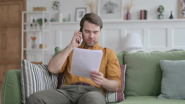Young Man Talking on Phone while Reading Papers on Sofa