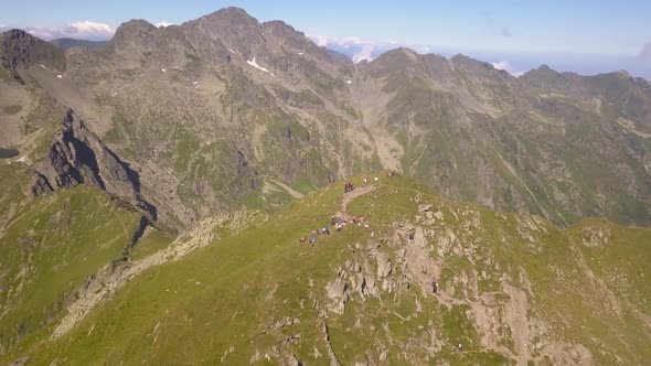 Drone orbiting high over remote mountain peak with hikers and backpackers on summit. Clear sky above