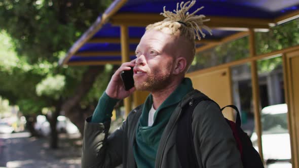 Happy albino african american man with dreadlocks in park talking on smartphone