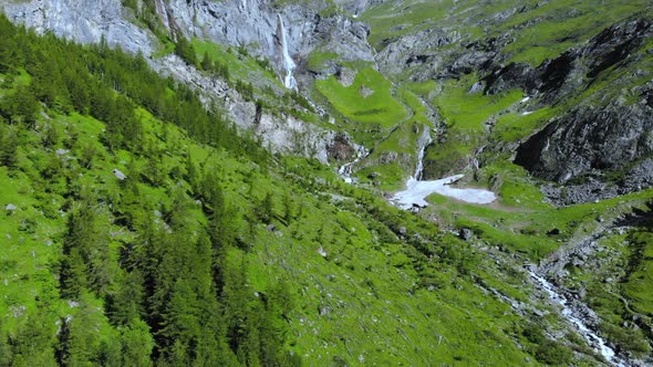 Aerial: drone flying over scenic high waterfall lush green valley and mountain stream on the Alps