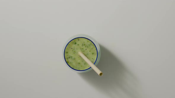 Hand Takes Blue Transparent Glass with Green Detox Smoothie on White Table with Paper Ecofriendly