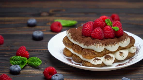 Portion of Classic Tiramisu Dessert with Raspberries and Blueberries on Wooden Background