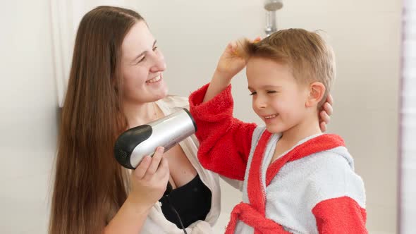 Portrait of Little Boy and Young Mother Drying Hair with Hairdryer in Bathroom