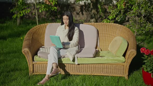 Wide Shot of Young Asian Beautiful Woman Sitting in Garden Waving at Tablet Web Camera