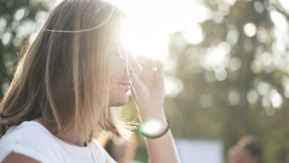 Closeup Caucasian Young Man in Sunrays Turning Looking at Camera Winking Putting Down Sunglasses