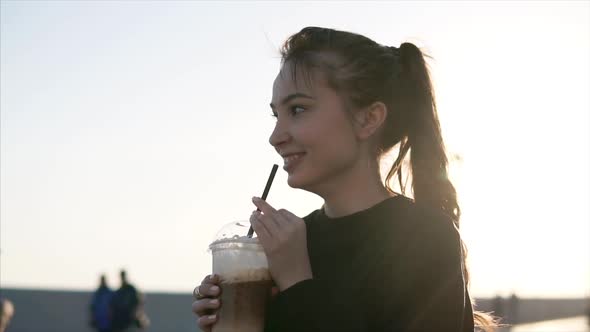 Cheerful Teenage Girl Is Sipping Cold Coffee on a Street in Evening