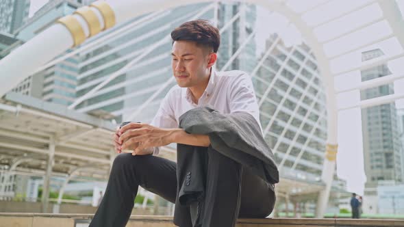 Asian unhappy business man sit at outdoor, feeling sad after unemployment from his job company.
