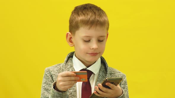 Caucasian schoolboy holds a bank card in his hands and a smartphone makes purchases online.