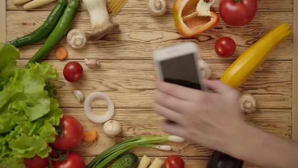The Man's Hand Puts the Smartphone on a Wooden Table with Vegetables