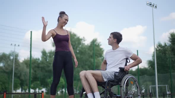 Joyful Young Girlfriend and Boyfriend in Wheelchair Gesturing Highfive in Slow Motion Laughing