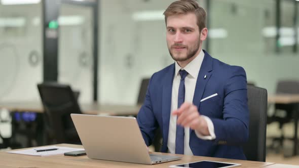 Businessman with Laptop Pointing at Camera