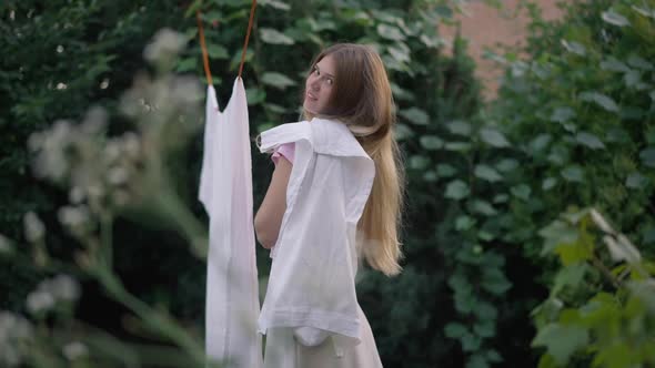 Side View Young Slim Woman Hanging Clean Fresh Laundry on Shoulder Smiling Looking at Camera