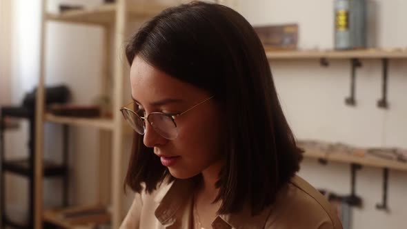 Closeup Face of Attractive Young Woman Artisan in Glasses Making Handmade Products at Table in