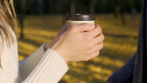Lovers warming their frozen hands with cup of warm beverage, autumn date