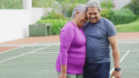 Video of happy biracial senior couple embracing on tennis court