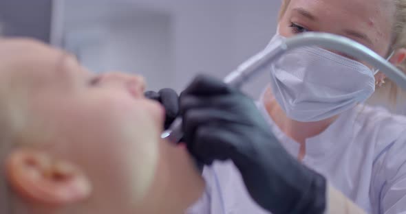 Female Dentist in a Medical Mask and Gloves Performs Dental Procedures in the Patient's Oral Cavity
