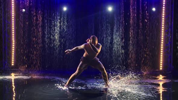 A Muscular Capoeira Acrobat Athlete Performs Tricks in the Pouring Rain, Creating a Lot of Water