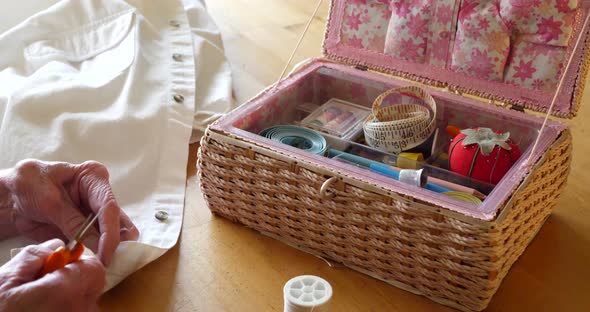 An old lady seamstress and her sewing kit as she cuts the thread of a button on a white dress shirt