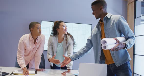 Three diverse male and female architects standing at table shaking hands in meeting room