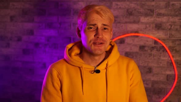 Young Man with Lavalier Microphone Talking on Camera Against Illuminated Brick Wall