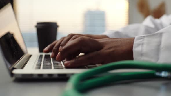 Closeup Hands of AfricanAmerican Male Doctor in White Coat Working Typing on Laptop Computer