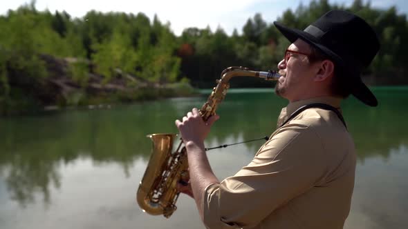 Jazz Musician Is Playing Saxophone on Shore of Lake in Forest, Medium Portrait