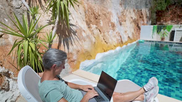 Side View Relaxing Adult Man Chilling By the Pool During Vacation at Resort Hotel Watching News or