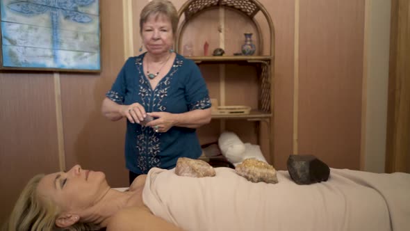 Energetic healer placing crystals on a mature woman’s body for crystal dowsing therapy.