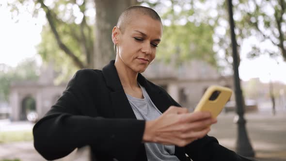 Positive bald woman typing by phone and looking around