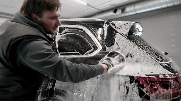 Closeup of a Man Washing a Black Car Covered with a Foam Using the Special Cleaning Glove