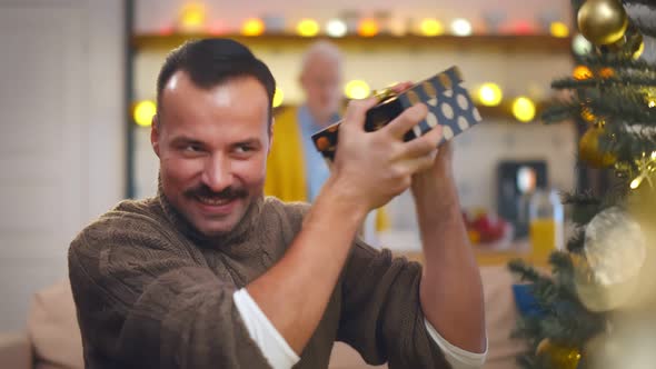 Smiling Man with Mustache Hooding Christmas Gift at Home