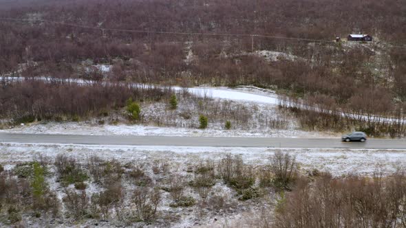 Cars Driving Through Dovre Mountain With Leafless Trees During Winter In Norway. - aerial pullback