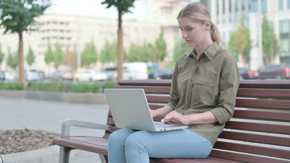 Woman Celebrating Success on Laptop while Sitting Outdoor on Bench