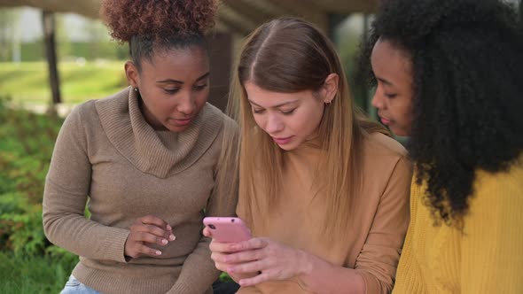 Close-up of three female friends showing each other photos on their phones