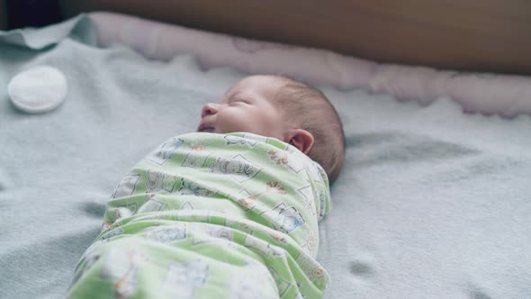 Newborn Baby with Closed Eyes and Fair Hair Lies in Swaddle