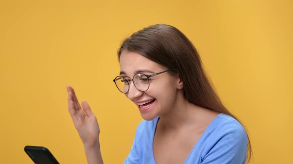 Closeup Overjoyed Woman in Eyeglasses Chatting Smartphone Having Good News Isolated on Orange Studio