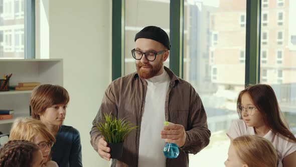 Close View of the Handsome Male Teacher Wearing Glasses and Hat Shows to the Pupils How to Watering