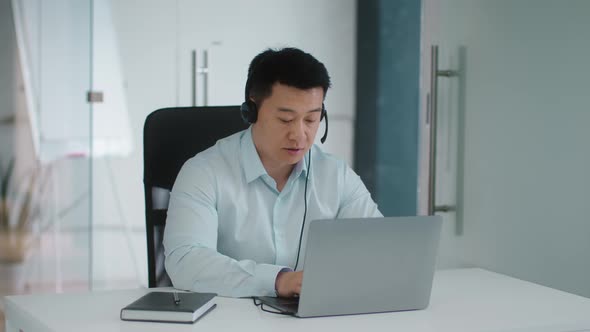 Professional Mature Asian Man Operator Wearing Headset Video Chatting with Client Via Smartphone