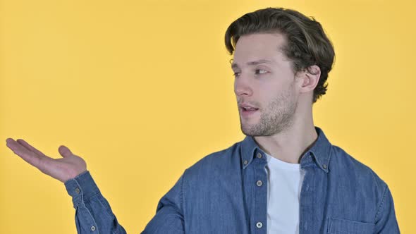 Young Man Holding Hand Out, Product Placement on Yellow Background