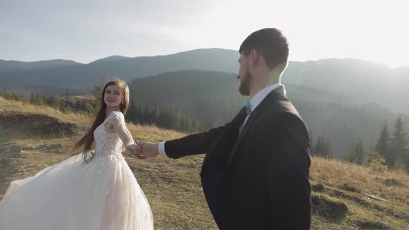 Newlyweds. Caucasian Groom with Bride Walking on Mountain Slope. Wedding Couple