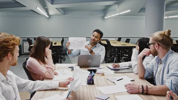 Ceo Man Showing Diagram Explaining Details of Startup Project to Diverse Colleagues Sitting at Table