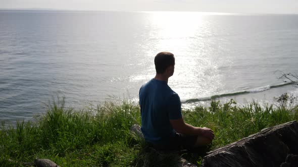 A fit young man in silhouette sitting and practicing meditation and mindfulness in a lotus pose in n