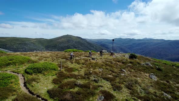 Drone video of 4 mountain bikers reaching the peak of a mountain top.