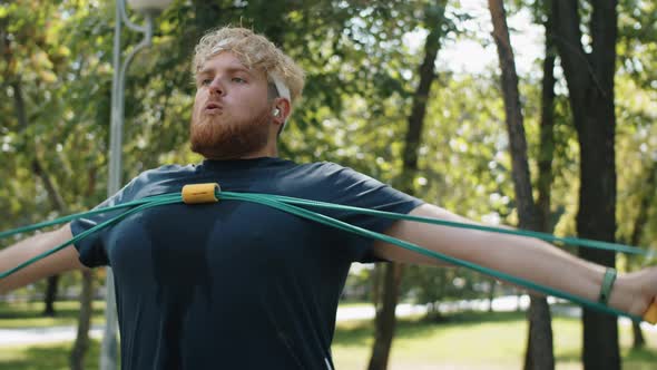 Overweight Man Exercising with Chest Expander in Park